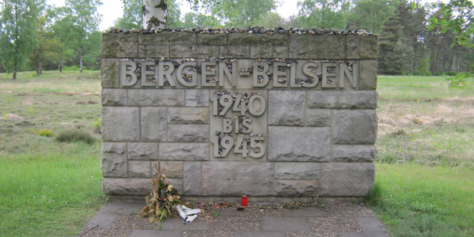 Steinernde Gedenktafel Bergen-Belsen mit grüner Wiese und Bäumen im Hintergrund.